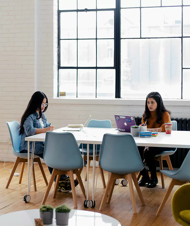 Two women seated at a table in a modern office setting.
