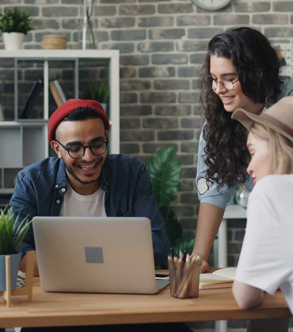 A group of three individuals gathered around a table, focused on a laptop in front of them.