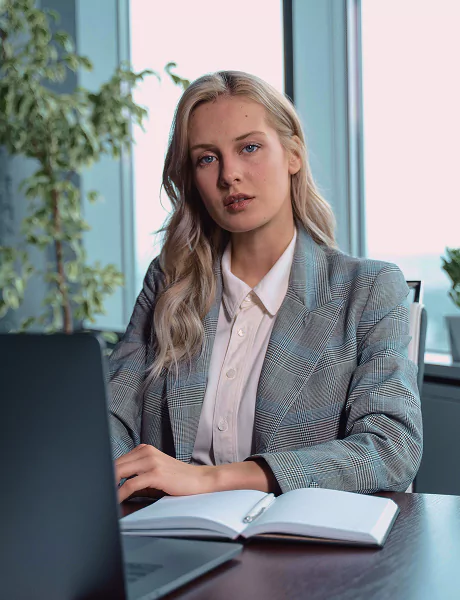 A woman in a suit sits at a desk, working on a laptop
